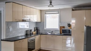 Et moderne køkken med lysegrå skabe, en sort bordplade, indbygget ovn, mikroovn og et vindue der giver naturligt lys.