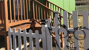 Een klein, twee verdiepingen tellend huis met een houten terras en een witte hekwerk.