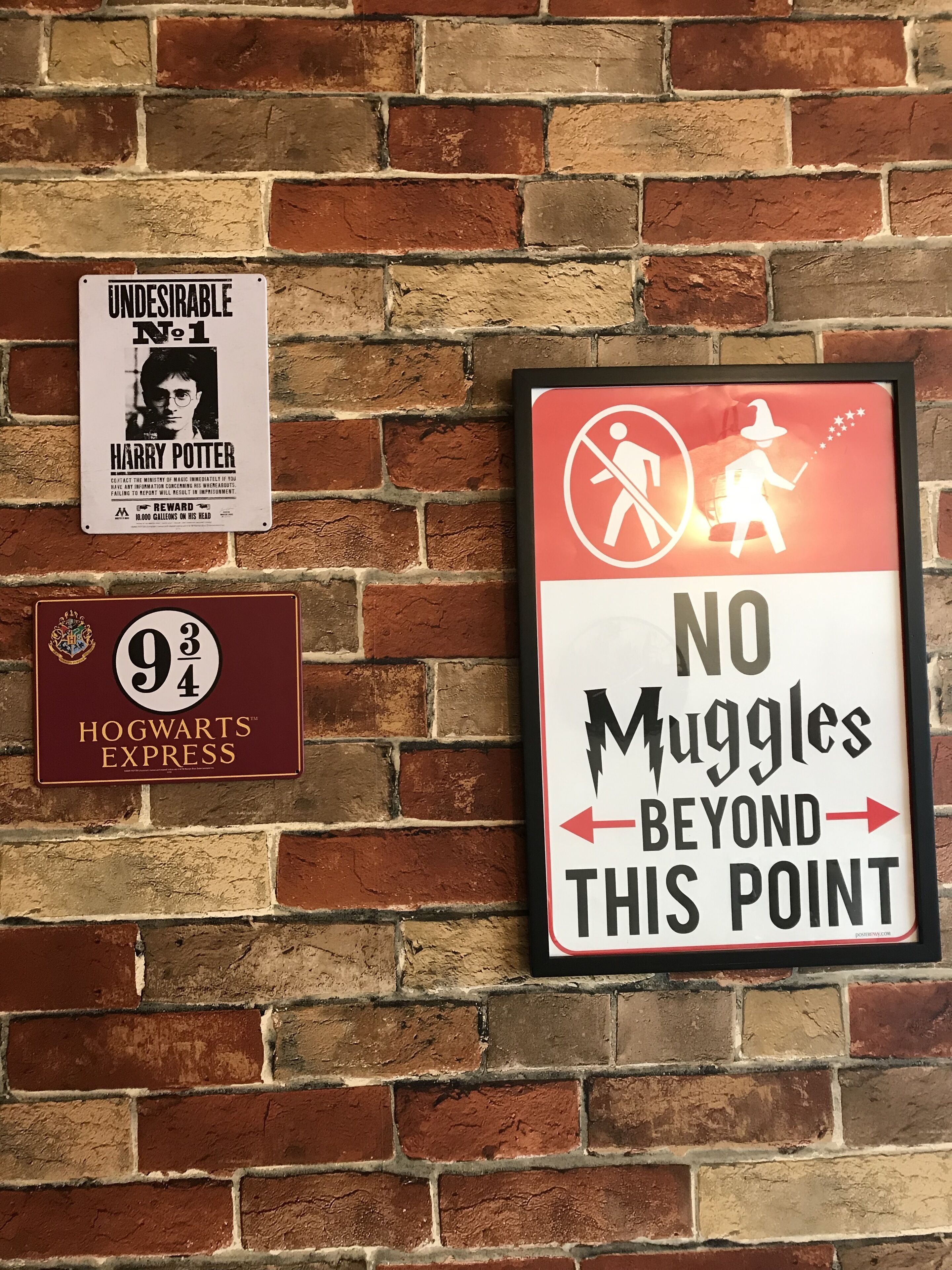 Drie borden aan een bakstenen muur: een bord met 'Harry Potter No. 1', een bord met 'Hogwarts Express' en een bord met 'Geen Muggel's hier verder'.