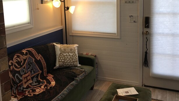 Een gezellige woonkamer met een groene bank, een houten plafond en een groot raam met jaloezieën.