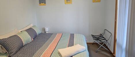A bedroom with a bed, a ceiling fan, a chair, and a window with curtains.