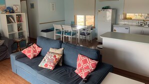 En stue med blå sofa, spisebord med stole, et køkkenområde og en loftsvifte.