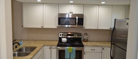 A kitchen with white cabinets, a stainless steel stove, a microwave, and a refrigerator.