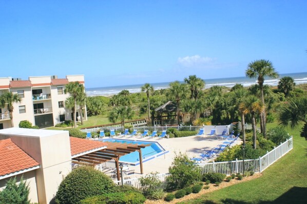 A resort with a pool area, beach chairs, and a view of the ocean.