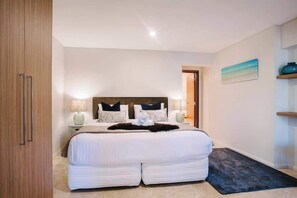 A hotel room with a large bed, bedside lamps, a painting on the wall, and a wooden wardrobe.