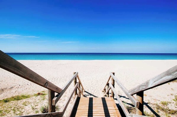 Een houten trap die naar een strand leidt, met een helderblauwe lucht.