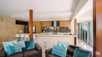 A modern kitchen with a central island, a dining area with a table and chairs, and a living area with a sofa and cushions.