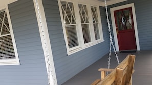Eine Veranda mit einer Schaukel, einer roter Tür und weiß gefassten Fenstern.
