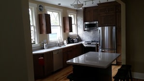 A modern kitchen with wooden cabinets, a stainless steel refrigerator, a microwave, and a gas stove. - Historic 1908 Downtown Home - Porch Swings - Mountain Views - Very Walkable (Asheville)