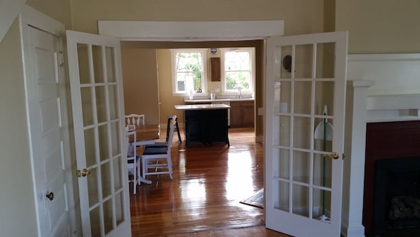 An open doorway leading to a kitchen with wooden flooring, a dining area with chairs and a table, and a fireplace. - Historic 1908 Downtown Home - Porch Swings - Mountain Views - Very Walkable (Asheville)