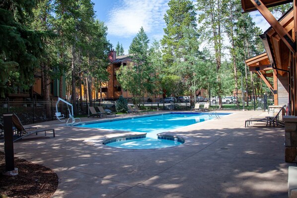 A swimming pool surrounded by lounge chairs and trees, with a building in the background.