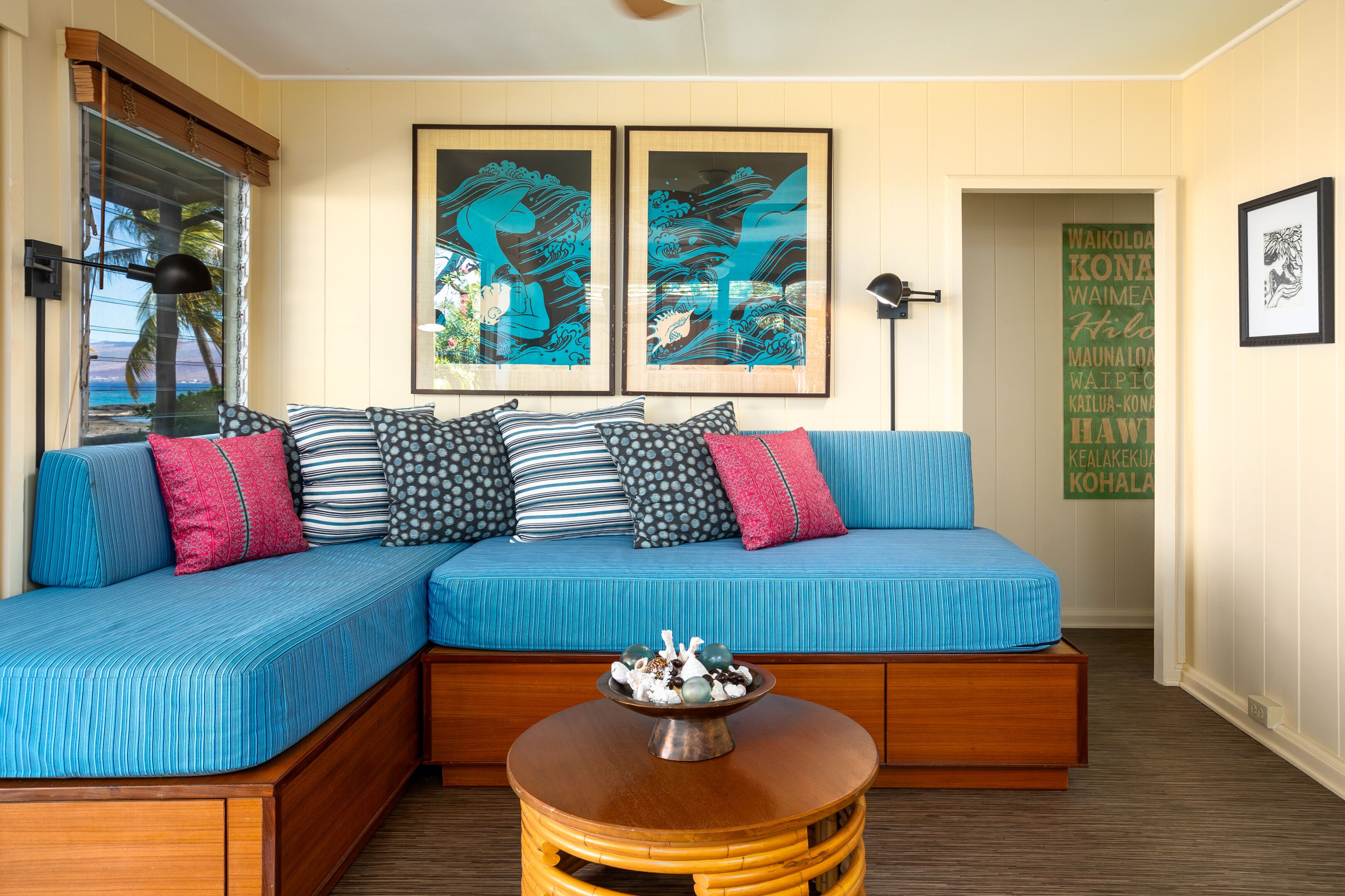 A room with a blue upholstered sectional sofa, a wooden coffee table, and artwork on the walls.