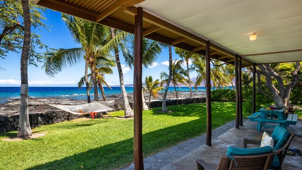 A covered outdoor area with a view of the ocean, a grassy lawn, and a table with chairs. - 'My Favorite Place on Earth' (Kamuela)