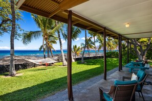 A covered outdoor area with a view of the ocean, a grassy lawn, and a table with chairs. - 'My Favorite Place on Earth' (Kamuela)