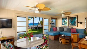 A spacious living area with a large window overlooking a beach, a ceiling fan, and a television on the wall. - 'My Favorite Place on Earth' (Kamuela)