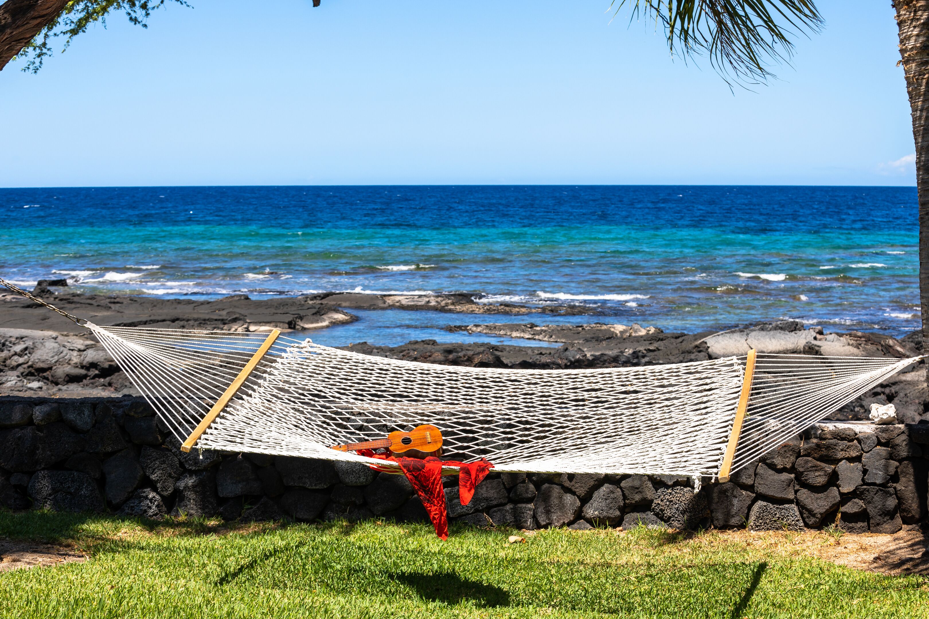 A hammock with a guitar and red cloth, set against a rocky shoreline and ocean view.