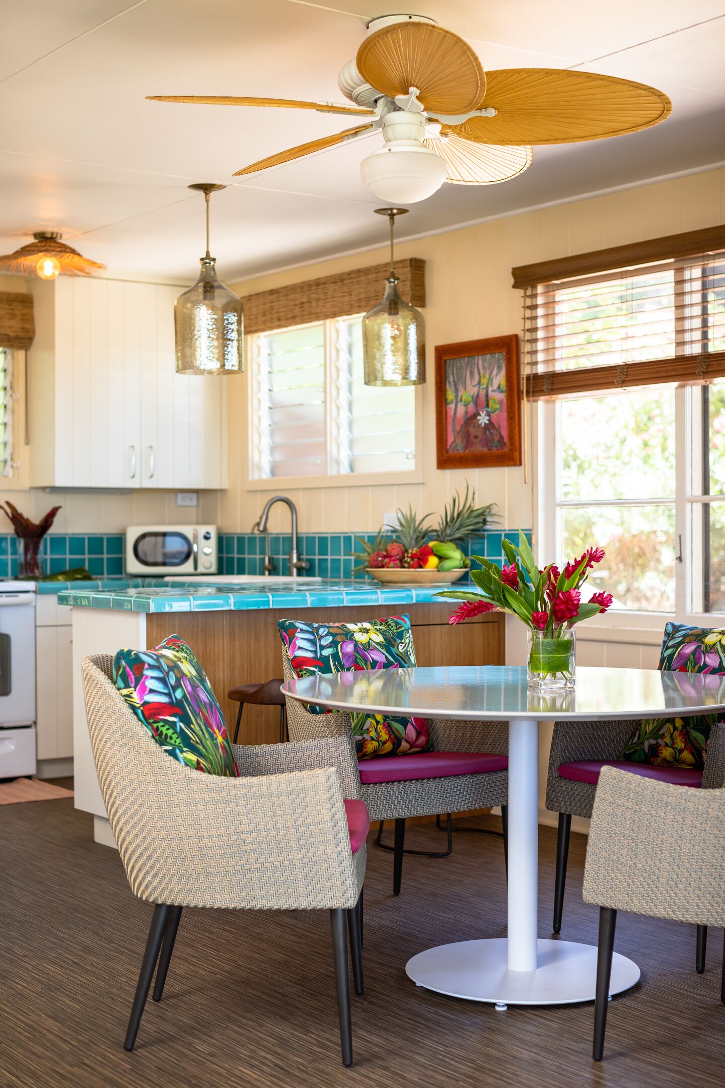 A kitchen with a dining area, featuring a round table, wicker chairs, a ceiling fan, and a microwave.