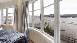 Habitació d'hotel amb una finestra gran que ofereix vistes a un riu i a les colines llunyanes.