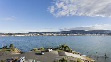 A waterfront parking area with vehicles, a clear sky, and a distant cityscape.