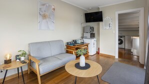 Un saló modern amb un sofà gris, una taula de centre de fusta, una petita taula auxiliar amb una làmpada, una planta en test i un televisor de pantalla plana fixat a la paret.