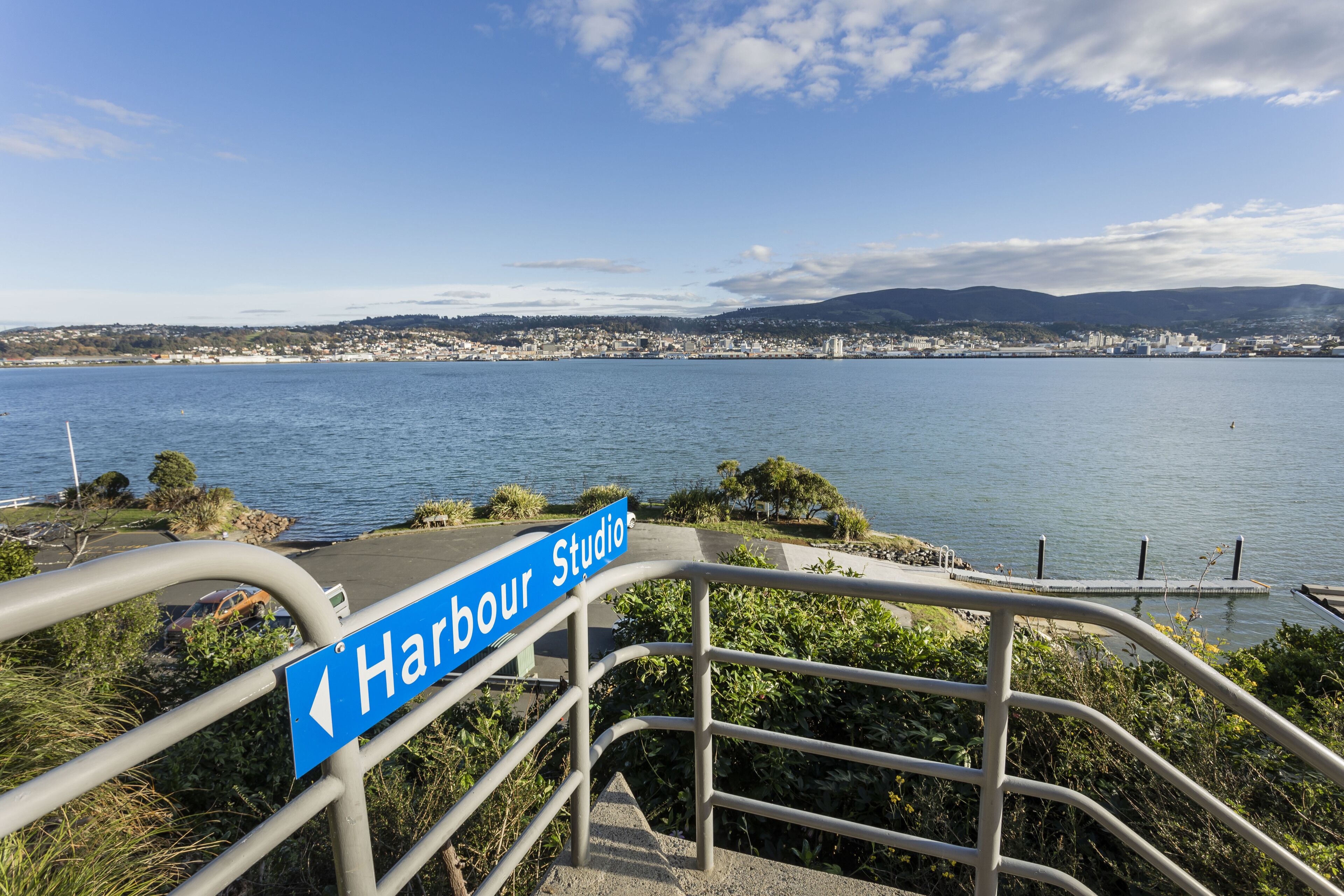 A sign for Harbour Studio with a view of a coastal city and water.