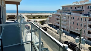 Un balcón con vista a la playa y un edificio rosado con balcones.
