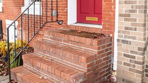 A red brick building with a red door, a white window, and a black metal staircase leading to the entrance. - Amazing location for conferences and ballgames with Free Parking! (Baltimore)