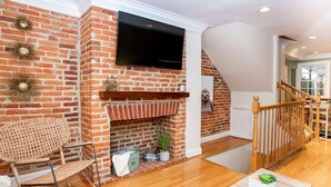 A living room with a brick fireplace, a mounted TV, a wooden rocking chair, and a staircase. - Amazing location for conferences and ballgames with Free Parking! (Baltimore)