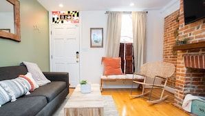 A cozy living room with a sofa, a rocking chair, a wooden coffee table, and a brick wall. - Amazing location for conferences and ballgames with Free Parking! (Baltimore)
