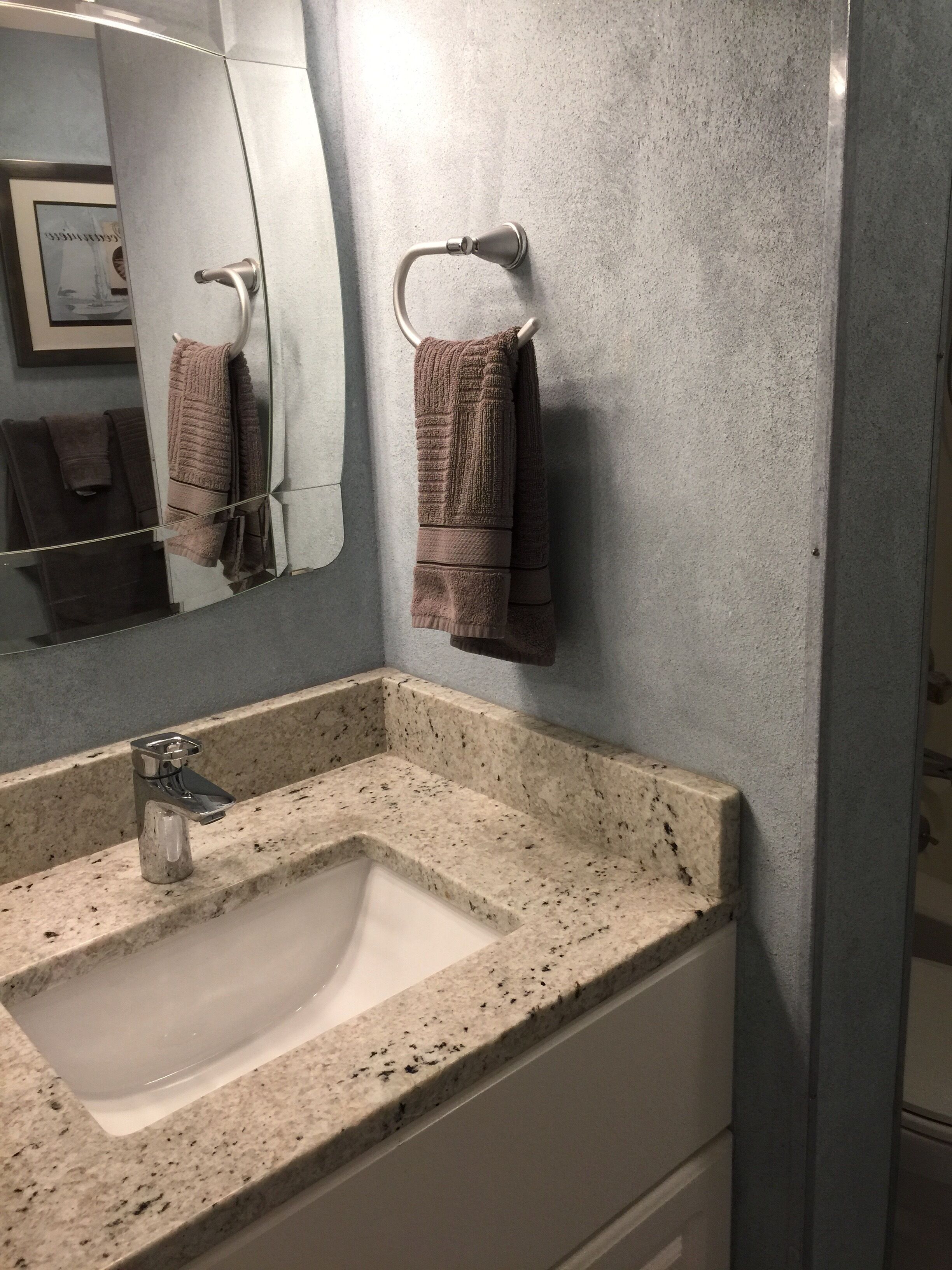 Une salle de bain avec un lavabo doté d’un plan de travail en granit, un miroir et deux serviettes suspendues à des crochets.