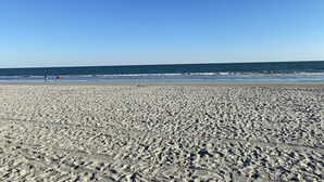 Ampia spiaggia sabbiosa con impronte che conducono verso l'acqua, cielo azzurro e mare calmo.