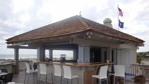 Zona bar all'aperto coperta con vista sull'oceano, con bancone, sedie bianche e una bandiera americana.
