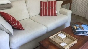 Una sala de estar con un sofá beige, una mesa de centro de madera, un espejo, una lámpara y una estantería.