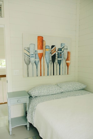 Une chambre à coucher comprenant un lit, une table de chevet et un tableau représentant des formes abstraites, accroché au mur.
