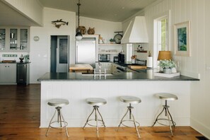 Una cocina amplia con una isla central, taburetes de bar, refrigerador y microondas.