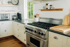 Une cuisine équipée d’une cuisinière en acier inoxydable, de meubles blancs, d’un plan de travail en bois et d’une fenêtre donnant sur un paysage verdoyant.