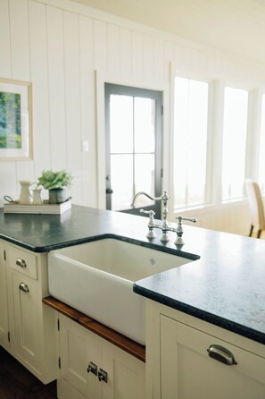 Une cuisine avec un évier blanc, un plan de travail foncé et des meubles bas en bois.