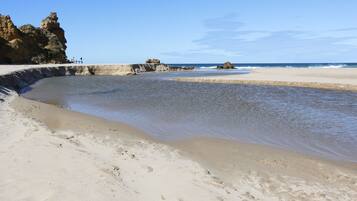Een zandstrand met rotsformaties en kalm water.