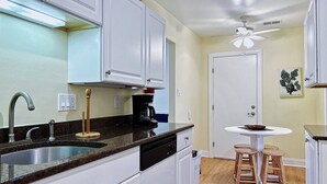 A kitchen with white cabinets, a black countertop, a sink, a coffee maker, and a ceiling fan. - Beautiful Bayside Gem Accepting 3 Night Stays! (Wildwood)