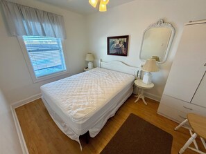 A bedroom with a bed, bedside lamps, a mirror, a dresser, and a window with blinds.