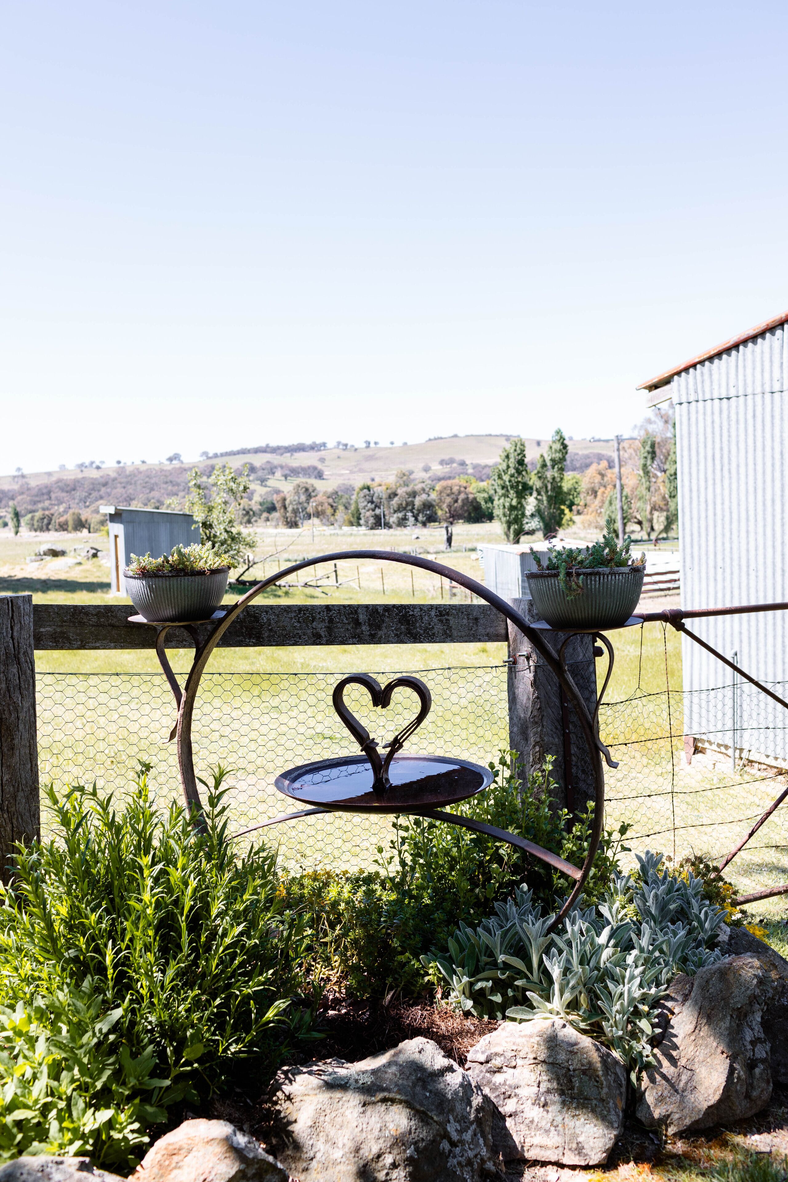 Un jardin agrémenté d’une table en métal et d’une décoration en forme de cœur, entouré de plantes et de rochers.
