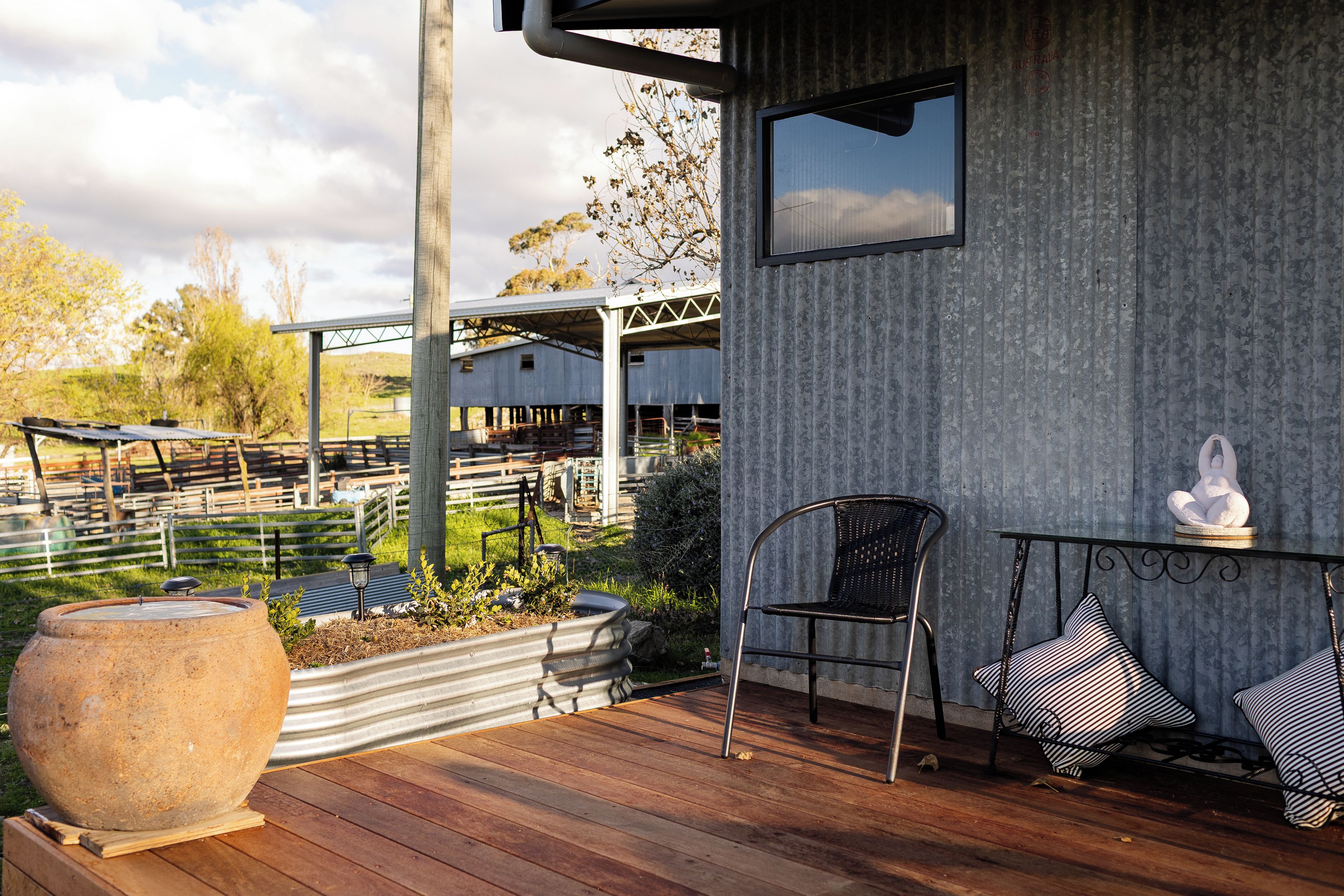 A wooden deck with a large stone planter, a metal chair, and a small table with decorative items.