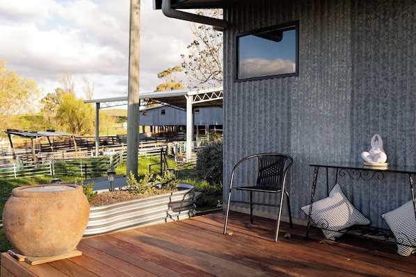 A wooden deck with a large stone planter, a metal chair, and a small table with decorative items. - The Quarters - A real farm experience (Emu Swamp)