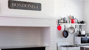Une cuisine avec un mur en briques blanches, une enseigne indiquant « BONDONGA », une cuisinière, un four à micro-ondes et divers ustensiles de cuisine.