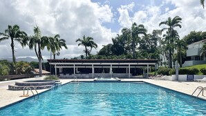 A swimming pool with a covered seating area, palm trees, and a view of mountains in the background.