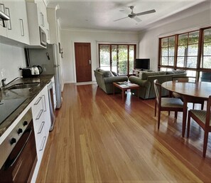 A spacious living area with a kitchen, wooden flooring, a dining table, and a large window providing natural light. - Tantallon in Berry - an exclusive getaway with wifi + pool (Bundewallah)
