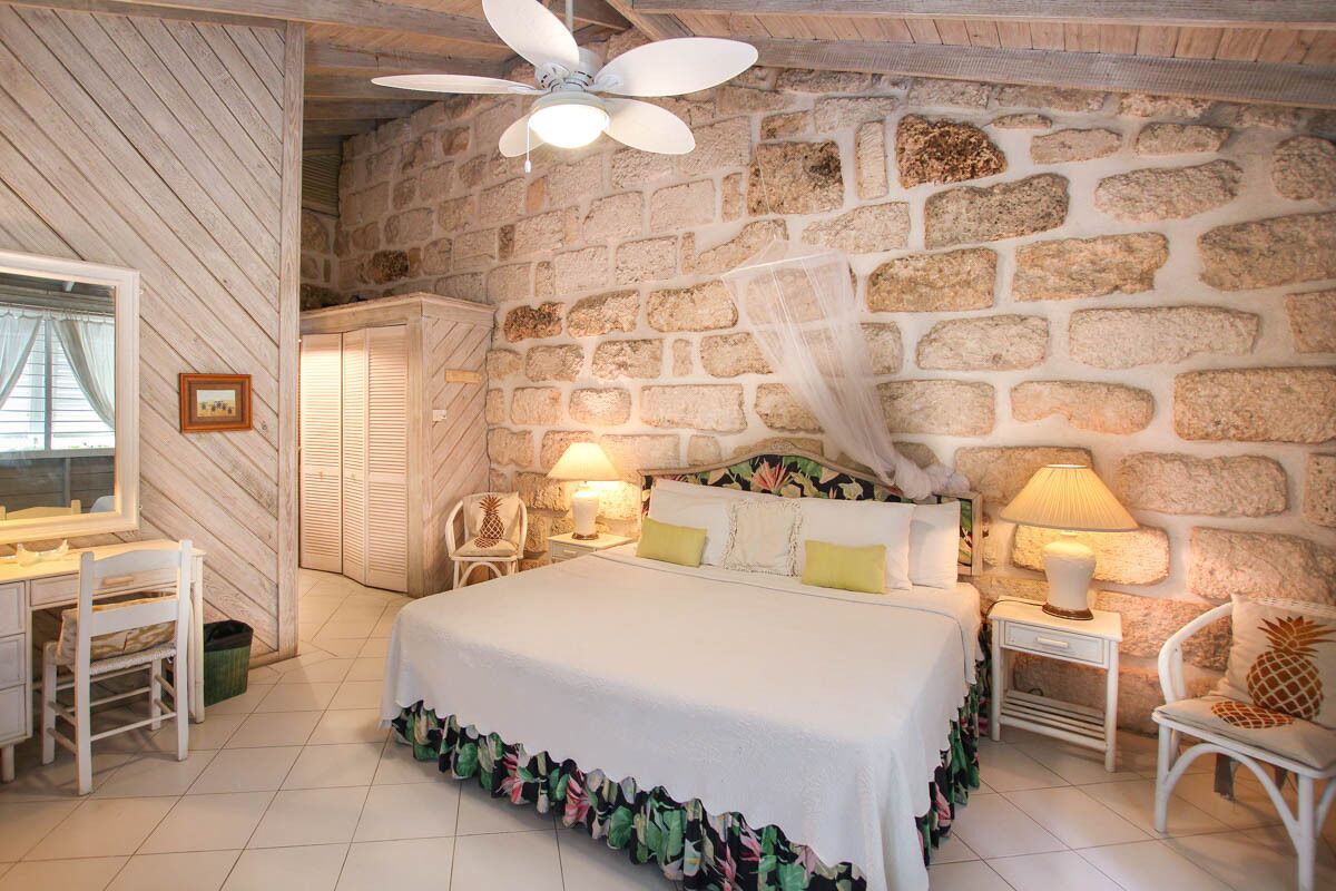 Una camera da letto con parete in pietra, un letto con copripiumino bianco, due abat-jour, una sedia e una scrivania con sedia.