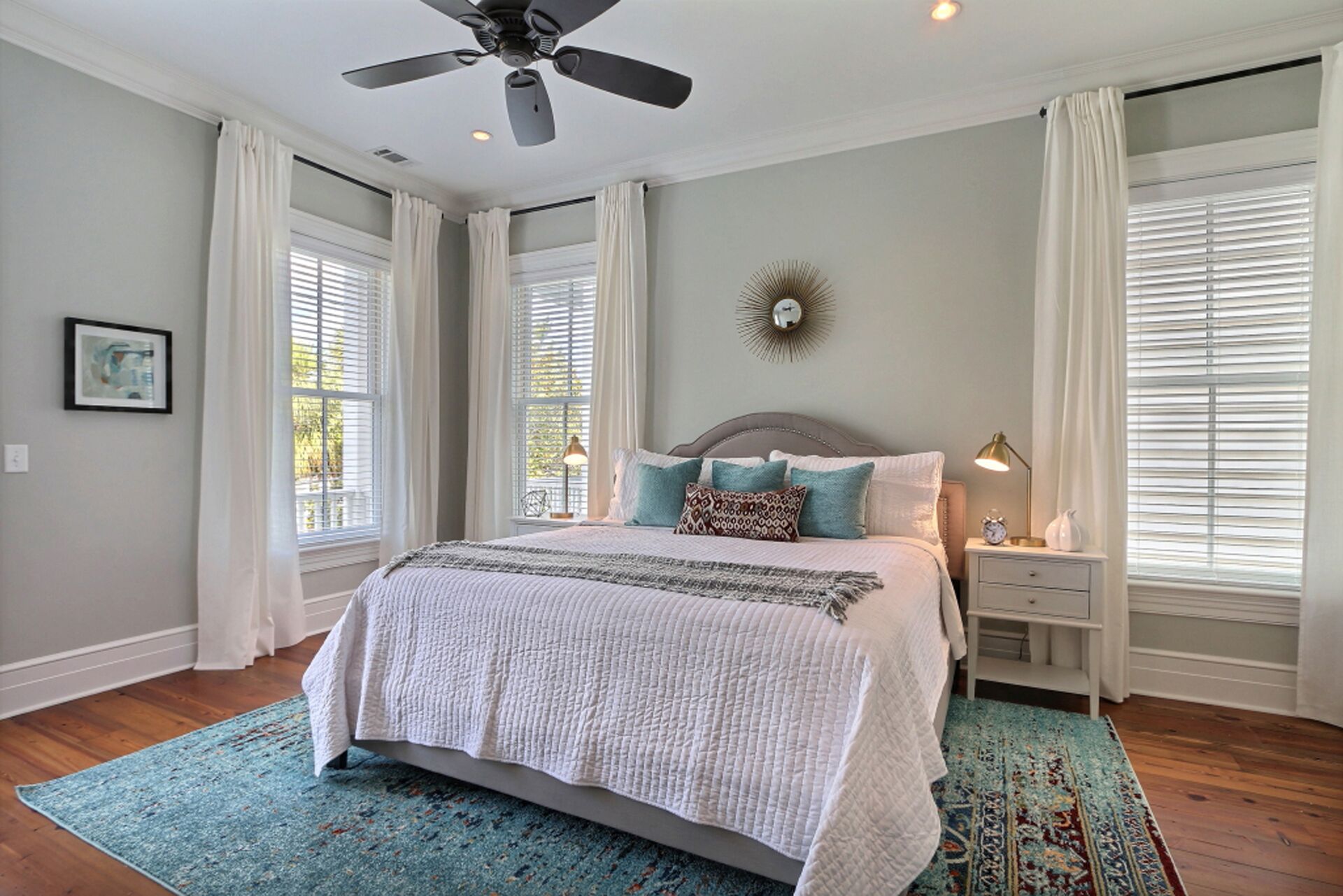 A bedroom with a bed, nightstands, a ceiling fan, and a large window with blinds.