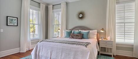 A bedroom with a bed, nightstands, a ceiling fan, and a large window with blinds.