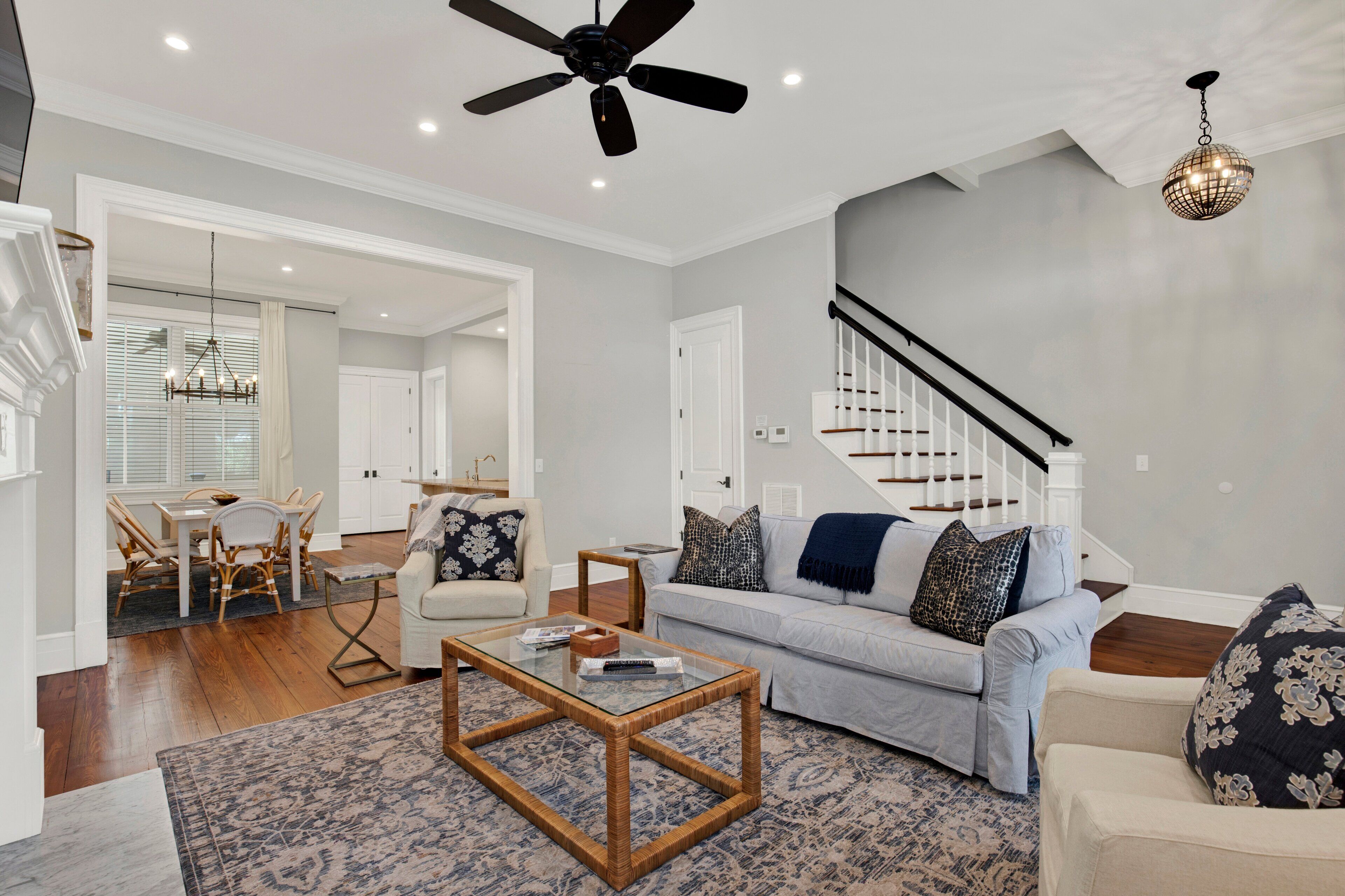 A spacious living room with a high ceiling fan, a staircase, and a dining area with a table and chairs.